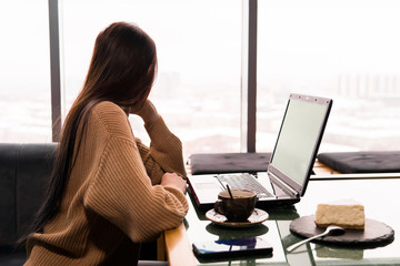 young woman with a laptop in a coffee shop thoughtfully looks out the window