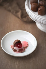 Chocolate covered cherries on white pedestal with brown background.  One isolated in front on white plate.