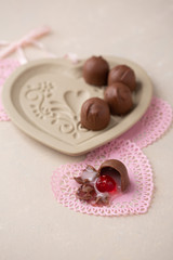 Chocolate Covered Cherries displayed in a heart shaped cookie mold.  One isolated in front on pink heart-shaped doilies.  Beige background with room for text.