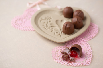 Chocolate Covered Cherries displayed in a heart shaped cookie mold.  One isolated in front on pink heart-shaped doilies.  Beige background with room for text.