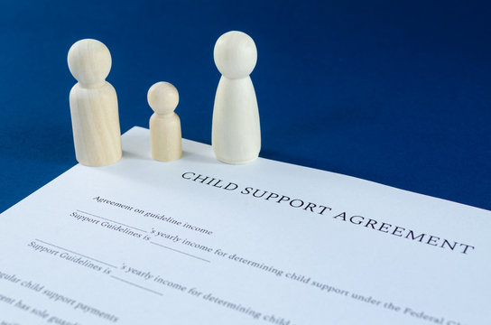 Printed child support agreement with man, woman and child wooden figures in a conceptual image for financial child support. Over blue background.