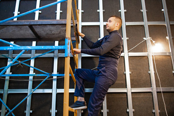 Worker climbs scaffolding. Making repairs in the room. Metal frame mounting on the wall. Home building and repair.