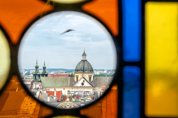 Upper part of St. Anne's Church - dome, towers and roof - in Krakow, Poland. View from the Town Hall Tower through window with colored stained glass windows. A bird flies in the sky.