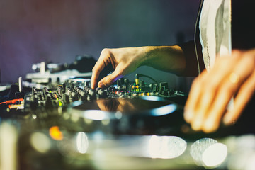 Dj playing music at mixer on a disco club close up on the hands and bokeh lights