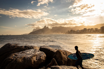 Surfer with surfboard in hand watching sunset at Pedra do Arpoador, Arpoador Beach, Rio de Janeiro,...