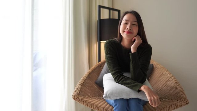 Lovely Beautiful Asian Woman Sitting on Chair By Window Holding Pillow and Looking To Camera With Smile, Static Copy Space