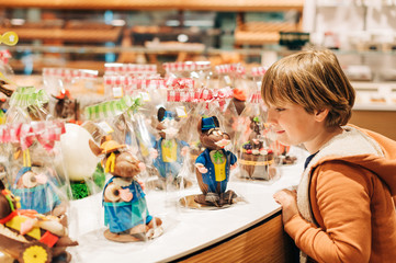 Funny kid boy admiring easter chocolate bunnies in chocolate shop