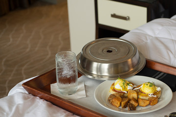 Room service in a hotel room with eggs Benedict, potatoes and water