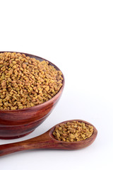 Fenugreek seeds in wooden bowl with spoon isolated on white background