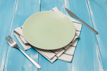 Green Plate with utensils and dish towel on blue wooden background with perspective