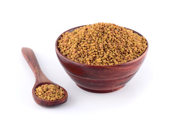 Fenugreek seeds in wooden bowl with spoon isolated on white background