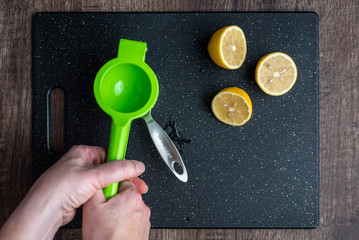 Woman’s hands using citrus squeezer to juice a lemon into a measuring cup, black cutting board