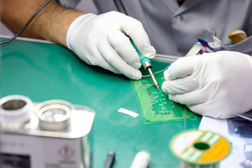 Close-up technician male on rubber gloves and work suit is using soldering to weld electronics  circuit board on office desk in factory. workshop on smart manufacturing