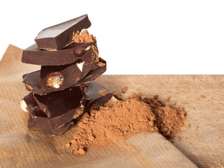 Broken dark chocolate bar with almonds and cocoa powder on beige paper surface