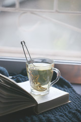 Knitted Sweater cup of hot tea Open Book on window. Cozy Winter Autumn day. Natural Light Authentic Tranquil Atmosphere. Kinfolk Hygge Slow Living Style. Matte Toned