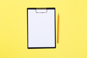 Clipboard with white sheet and pen on a yellow background. View from above. space for text