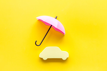 Car insurance. Automobile toy under umbrella on yellow background top-down copy space