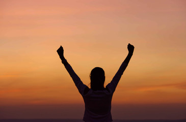 The black silhouette of behind the women raise their arms Background sky orange light of sunset.