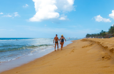 Back view of young family with a little daughter walking along the beach together holding hands