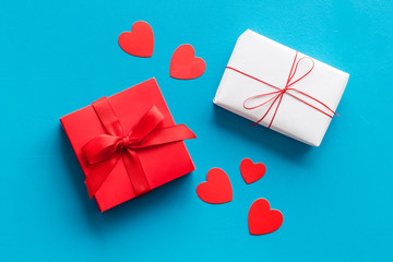 Present to a lover on Valentine's Day. Gift boxes near paper hearts on blue background top-down.