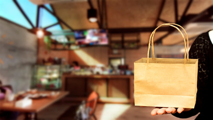 Hand holding paper bag with on coffee shop blured background