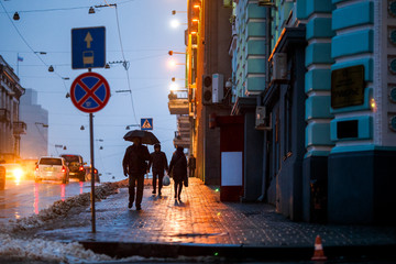 Rainy weather in the city. People walk under umbrellas during light rain on the wet streets of the...