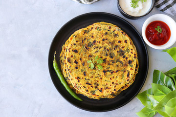 A Food called Methi paratha or Methi thepla is a Indian breakfast dish served with curd and ketchup. with copy space.