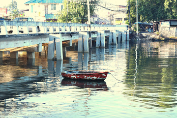 Fototapeta na wymiar The image of an old small boat floating on a river under the cement bridge. In Chonburi, Thailand