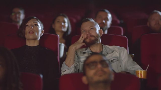 Tracking shot of man and woman watching sad movie at cinema and crying