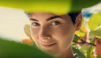 Beauty Woman Face With Green Leaves Around Face. Skin care, pure beauty, cosmetics concept .Young green-eyed girl looking through leaves, closeup.