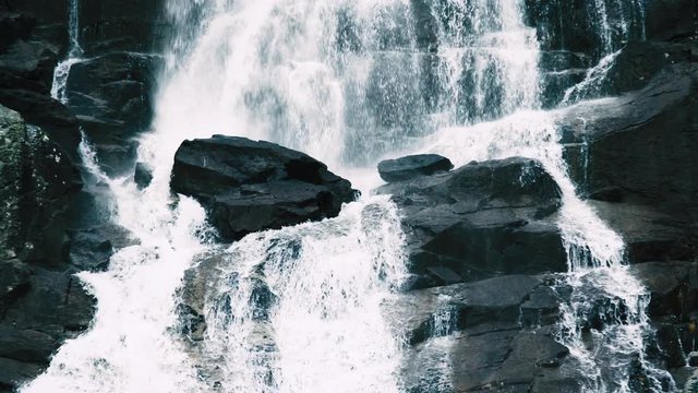 Long slow-motion footage of waterfall with streams gushing down by bare stones rapidly