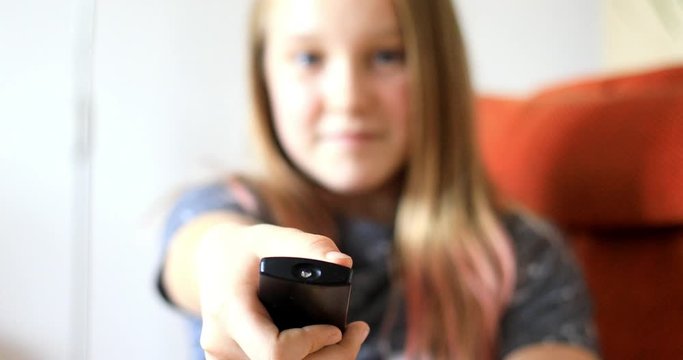 Young girl switches programs. Child with remote on TV. Focus on remote control, person in background intentionally out of focus.