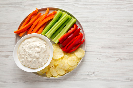 Homemade Caramelized Onion Dip with Potato Chips, Celery, Pepper and Carrot on a white wooden background, top view. Flat lay, overhead, from above. Copy space.