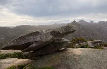 There is a viewpoint near the city of Ezaro in Galicia in northern Spain. There are interestingly shaped rocks. The stone in the foreground looks like a turtle. Mountains and clouds in the background.
