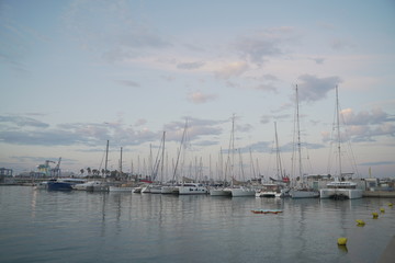 Naklejka premium Luxury power boats in the Royal Marina in Valencia Spain, some moored,others sail on the sea. The city of Calpe in Spain, Valencia, Europe, in the cloudy evening 
