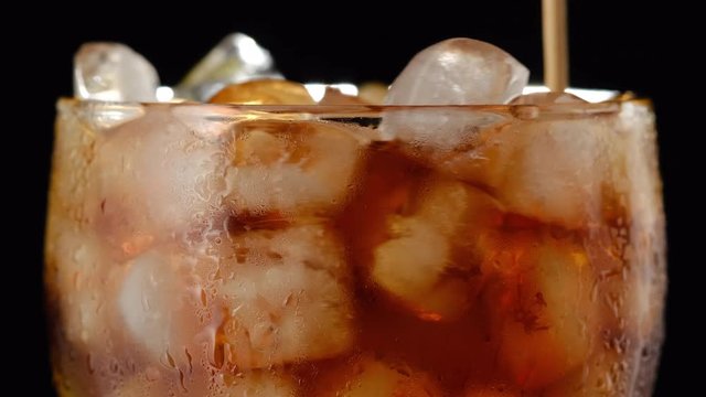 mixing cocktail Сuba libre with ice and lime in a cold glass with bubbles and water drops. Glass of Cola drink with Ice and bubbles and water drops on glass. Soda closeup.
