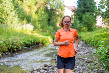 Girl in a bright orange T-shirt running along a mountain river.
