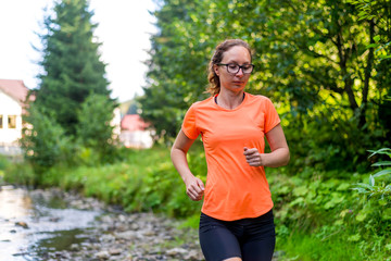 Girl in a bright orange T-shirt running along a mountain river.