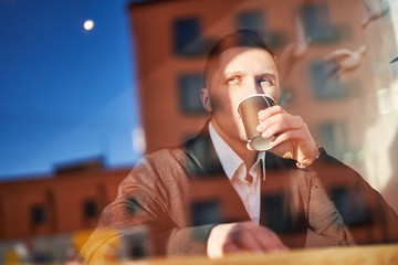 Man drinking from glass sitting in cafe, reflection of building