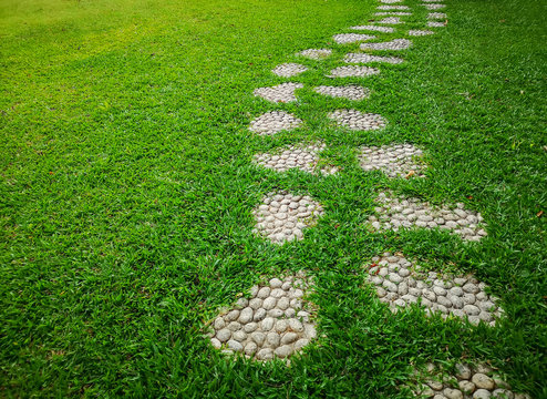 Curve pattern walkway of gravel stepping stone on fresh green grass yard, smooth carpet lawn in the public park
