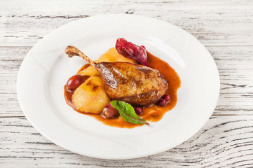 Confit duck leg in a restaurant close-up. Duck leg with pear in wine on a white plate and copy space.