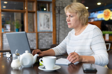 A woman with a laptop looks at a document in a cafe, office
