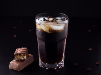 iced coffee on a black background next to coffee beans with a chocolate bar