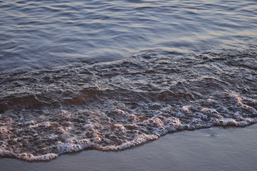 Photo of a beautiful sunny day. Late evening, sunset, tide. A beautiful strong wave runs on the sandy shore of the sea.