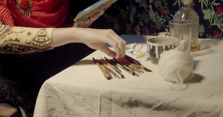 Close up of Frida Kahlo using palette while painting, sitting at the table, 4k