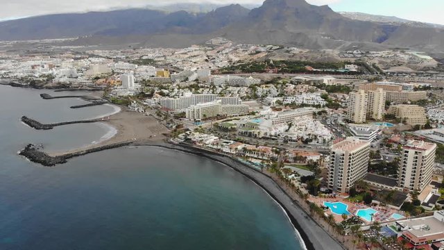 Aerial panoramic view of Las Americas city, Tenerife, Canary islands. Cinematic 4K footage with black volcanic rocky coast, Atlantic ocean, city modern villas, beaches, mountains. Bird eye shot