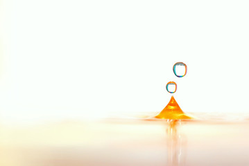 two stylish multi-colored waterdrops splashing on a orange water bowl on bright white background