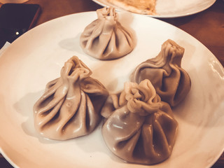 Tasty white traditional large flour Georgian round khinkali steamed lie in a plate on a wooden table in a cafe.