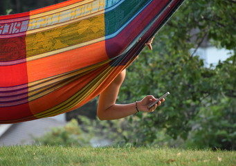 Girl lying in the hammock and using her smartphone in the garden