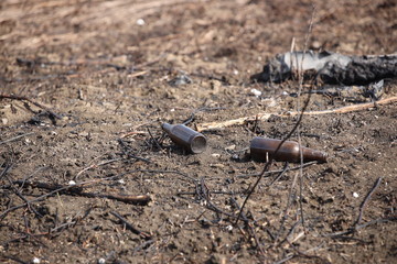 An empty glass charred bottle is lying on grass that has been baked out. Ecological catastrophy. Spring tan green cover. Danger of fire. The destruction of life and pollution. Problems of civilization